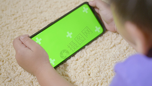 拥有在手机上玩数字电子游戏的小男孩儿童学前班白色屏幕房间视频学习互联网电话工具细胞绿色图片