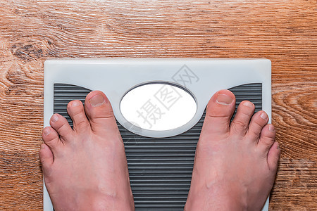 一个男人赤脚站在地板上 测量他的体重和体重图片
