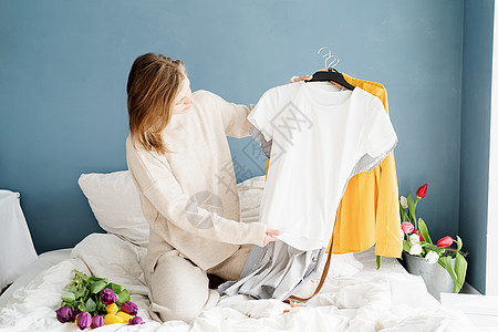 青年妇女在家里的床上整理衣服 安排她们穿的衣服洗衣店折叠家庭衣柜回收毛巾篮子花朵房间家务图片
