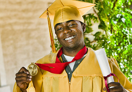 毕业日获得文凭和奖章的充满自信的男学生肖像图片