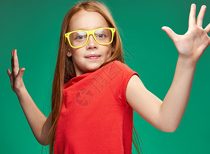 带着双手的黄色眼镜手势的可爱红头发女孩儿童年情感 绿色背景图片