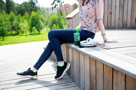 夏天坐在公园木制讲台上的年轻女孩被剪切的景象排毒呼唤食物衣服果汁高中杯子休闲装女性手机图片