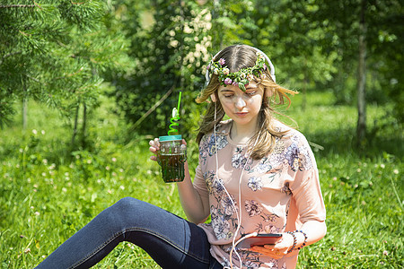 一个年轻女孩看着她的手机 坐在草坪上写留言 笑声女儿饮料衣服电话高中杯子果汁营养成人大学图片