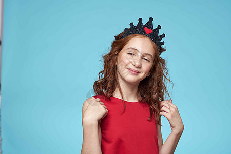卷发女孩 头戴皇冠的红礼服 生活方式蓝色背景孩子童年幸福女性工作室姿势女士闲暇青春期微笑图片