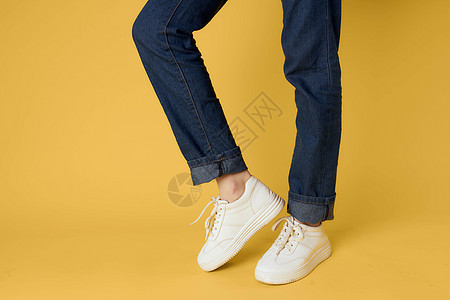 妇女腿上穿牛仔牛仔牛仔裤的白色运动鞋 时装街头风格 黄色背景图片