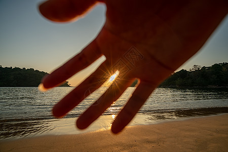 太阳在海面上空的橙色天空上 有人手举起头来阻止摄像头图片