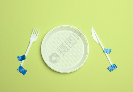 绿色背景上粘有蓝色胶带的一次性塑料叉子和勺子 避免塑料 保护环境图片