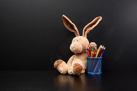 可爱的兔子坐在黑粉笔板的背景上 回到学校广告牌娃娃木板木质黑色毛皮教育玩具童年空白图片