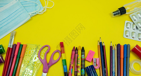 学校用品 如铅笔剪刀薄纸橡皮冲水标尺 彩色防水面具 黄色背景的酒精净化剂 在带有复制空间的可食性流行病期间返回学校概念隔离粉笔课图片