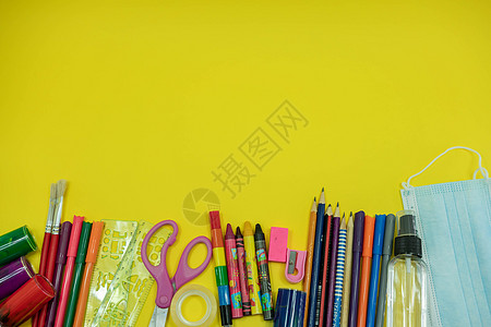 学校用品 如铅笔剪刀薄纸橡皮冲水标尺 彩色防水面具 黄色背景的酒精净化剂 在带有复制空间的可食性流行病期间返回学校概念塑胶安全预图片