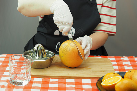一位年轻女子用手工果汁机做的橙子和葡萄油做新鲜的榨汁玻璃美食烹饪手套季节柚子家庭女士维生素水果图片