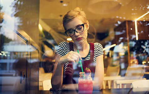 穿着红遮阳服的时装女人坐在咖啡厅里 照镜子玻璃反射街上的汽车技术咖啡店杯子互联网上网店铺酒吧城市学生咖啡图片