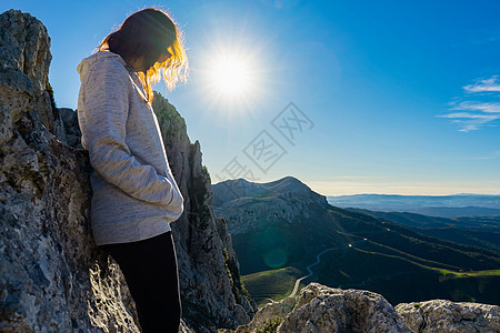 孤独的女人发现自己靠在山顶大自然中的岩石上沉思 山下有壮丽的景色 阳光透过她的头发 积极孤独的概念 找到自己的方式图片