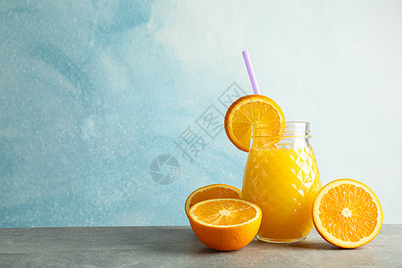 灰色桌子上装有新鲜橙汁 小管和橙子的玻璃罐 背景为彩色 文字空间 新鲜天然饮品情调作品饮料食物饮食木板榨汁机异国排毒水果图片