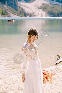 在意大利的上 美丽的新娘穿着带袖子和蕾丝的白色连衣裙 带着黄色的秋天干花和牡丹玫瑰花束 在欧洲的目的地婚礼 在 Braies 湖图片