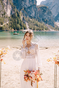 在意大利的 美丽的新娘穿着带袖子和蕾丝的白色连衣裙 在拱门的背景上放着一束黄色的秋天花束参加仪式 在欧洲的目的地婚礼 在 Bra图片