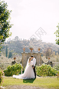 新娘和新郎在公园散步 在意大利托斯卡纳的一座古老的酒庄别墅举行婚礼 意大利古建筑前装饰着白色花朵和绿色植物的圆形婚礼拱门女士金发图片