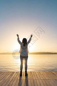 受太阳启发的年轻女子在日落或黎明时张开双臂望向大海 精神女孩背光中的后视剪影感谢上帝在宗教手势位置图片