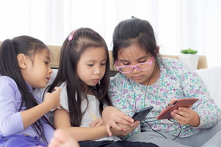 快乐的亚洲小孩和朋友在家里的沙发上玩智能手机 孩子们在沙发上一起使用手机 女孩看智能手机以获得娱乐 生活方式和沟通理念冲浪视频互图片