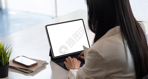 在空白屏幕的平板电脑上打字并坐在同事旁边的女商务人士手的裁剪照片图片