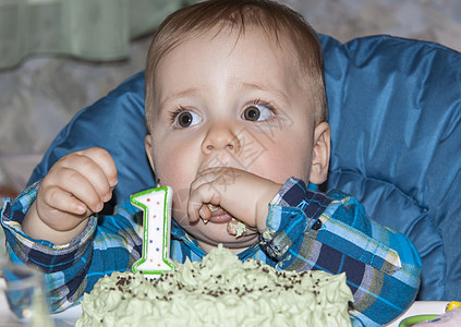 一个漂亮的婴儿庆祝他的第一个生日 并用手吃蛋糕 在孩子面前的桌子上放着第一的蛋糕问候语奶油微笑礼物食物问候甜点乐趣快乐假期图片