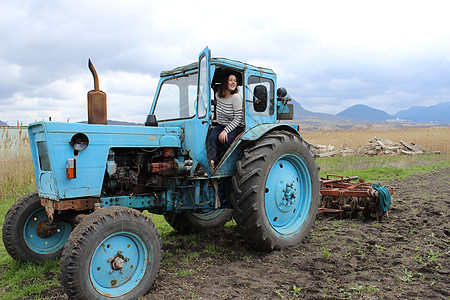 拖拉机上的女孩在田里 秋天把拖拉机的地耕种 农业工作土地装备青年农作物空气运输母猪收成图片