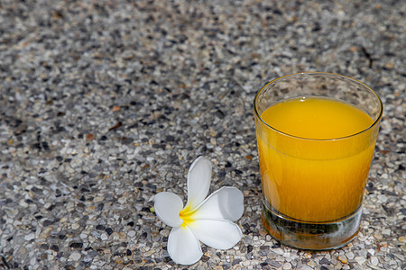 一杯新鲜的橙汁和鲜花 在石料背景上做点心教育玻璃晴天鸡蛋花桌面温泉配件假期桌子反射图片