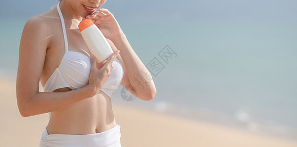 穿着白比基尼白色比基尼的女子在海滩上手里拿着防晒霜瓶身体泳装护理洗剂阳光晒黑润肤晴天日光浴皮肤图片