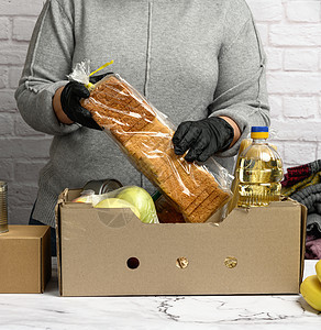 身穿灰色毛衣的妇女将食品包装在纸箱中 援助和志愿行动的概念产品捐款团结瓶子水果手套女士机构服务福利图片