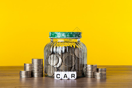 在有黄色背景的玻璃罐中有很多硬币 保存汽车概念图片