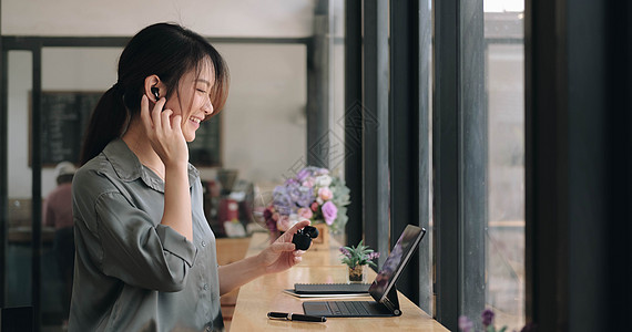 亚洲年轻女孩的特写使用无线耳塞在咖啡馆通过笔记本电脑进行在线语言课程和搜索信息图片