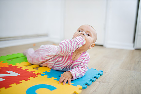可爱的婴儿躺在一席多彩的垫子上 嘴里握着拳头字母微笑女性女儿连衣裤尿布幸福喜悦黑发女孩图片