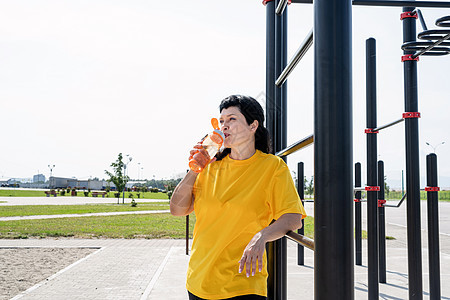 在运动场户外锻炼后 对高龄妇女饮用水进行微笑女性运动装身体活动老年福利退休单杠闲暇女士图片