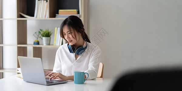 一位年轻漂亮的亚洲女性坐在家里的桌子和笔记本旁 用笔记本电脑在线学习的画像作家学校男人日记笔记办公室学生商业文档女士图片