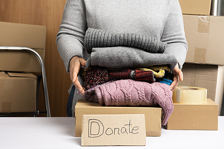 身穿灰色毛衣的妇女将衣服包装在盒子里 援助和志愿行动的概念服务社区捐款机构送货帮助白色女士女性纸板图片