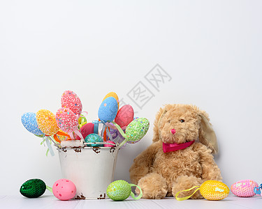 坐在白色背景和装饰多彩的东面鸡蛋上的玩具兔子娃娃假期绿色风格童年季节性动物季节庆典粉色图片