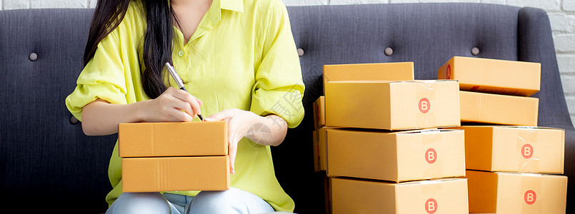 年轻的亚洲女性在家里的包裹箱上写地址 以便向客户 运输和物流 在线商家和卖家 企业主或中小企业 在线购物和电子商务订购送货单女孩背景图片