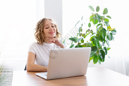 商业妇女使用笔记本电脑坐在办公桌白色办公室内部附近 家庭种植一边看工具电话居家视频互联网窗户女士职场自由职业者职业图片