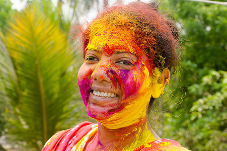 在 Holi 色彩节期间 一位年轻的印度快乐女人的肖像 脸上涂着粉黄色和红色的 Holi 彩色粉末涂料 正视图 看着相机节日色彩图片