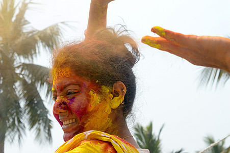 在 Holi 色彩节期间 一位年轻的印度快乐女人的肖像 脸上涂着粉黄色和红色的 Holi 彩色粉末涂料 正视图 看着相机乐趣色彩图片