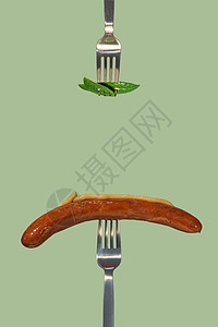 用叉子采摘的绿色鲜叶作为新的素食食品和烤香肠 在另一把叉子上放上芥末酱 色拉色纯色背景 带有文本 特写 细节的复制空间图片