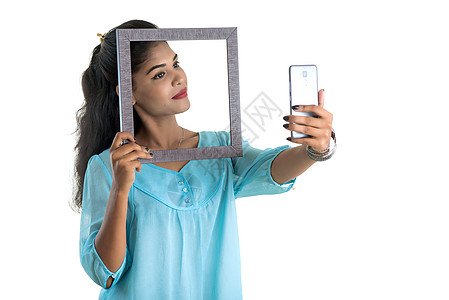 白色背景上使用带相框的手机或智能手机的印度年轻女孩框架商业女性展示药片屏幕庆典自拍女士技术图片