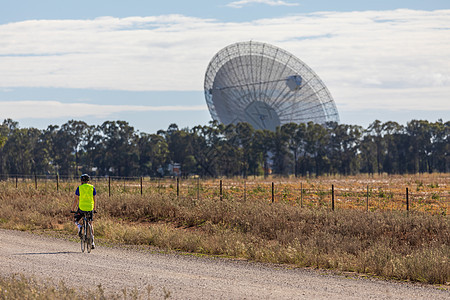 一个双环骑手接近一个大型室外科学射电望远镜背景图片