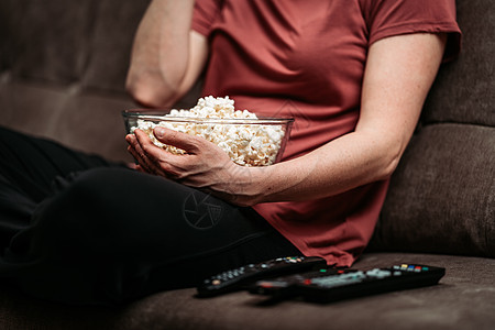 在电视上看电影时 还加了爆米花 遥控沙发玉米电影控制女性小吃消费者长椅娱乐时间喜悦图片
