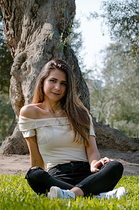 坐在公园一棵树下 坐着的棕发美女头发棕色太阳娘娘腔绿地相机草原混血女性裙子图片