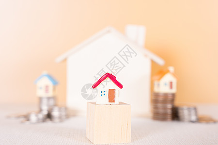 木块上的房子和堆叠硬币隔离橙色背景 存钱和投资概念图片