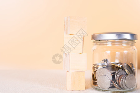 木块堆和罐子里的硬币隔离橙色背景 存钱和投资概念图片