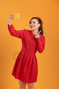 一位快乐的亚洲年轻女子拿着手机拍自拍 而她却站在橙色背景上与世隔绝电话技术女性细胞女孩成人互联网照片社会图片