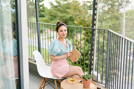 年轻有吸引力的亚洲女孩 在阳台上读书椅子玻璃桌子生活学习阅读寒意房子女士绿色图片