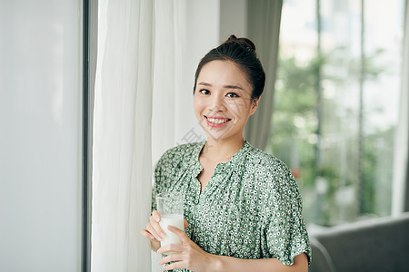 亚洲女士一边喝牛奶一杯 一边看着窗外的复制空间幸福白色牛奶杯子女性早餐成人房间窗户图片